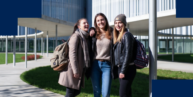 Tre studentesse sorridono abbracciate davanti a un edificio del campus