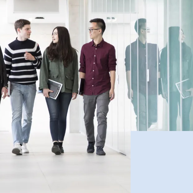 Tre studenti camminano lungo un corridoio vetrato del campus, con i libri sotto braccio