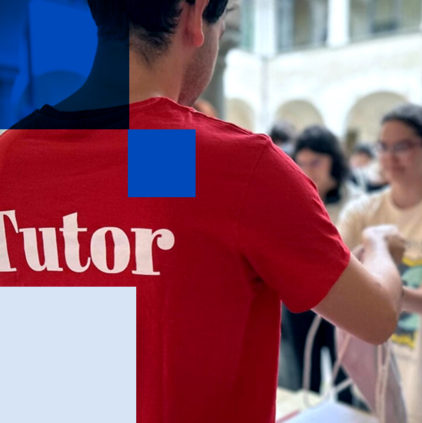 Un tutor di spalle, con la maglietta rossa, accoglie gli studenti a un banchetto